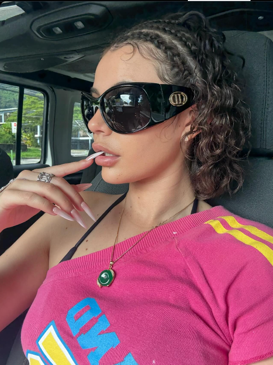 Woman wearing sunglasses and a pink top with yellow accents inside a vehicle.
