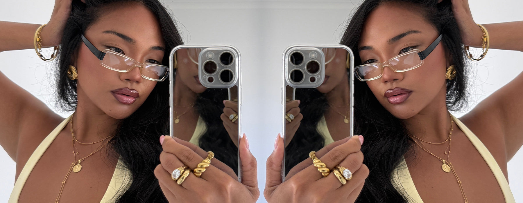 Woman holding up a phone with a clear case, wearing gold jewelry.