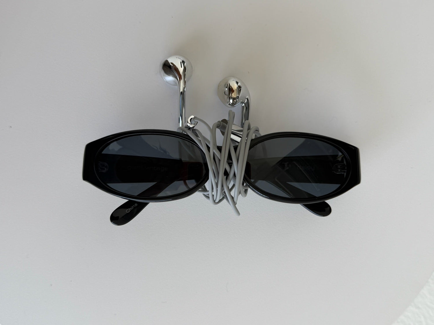 Black sunglasses with a unique geometric frame design, wrapped in a silver wire display stand on a plain white surface.