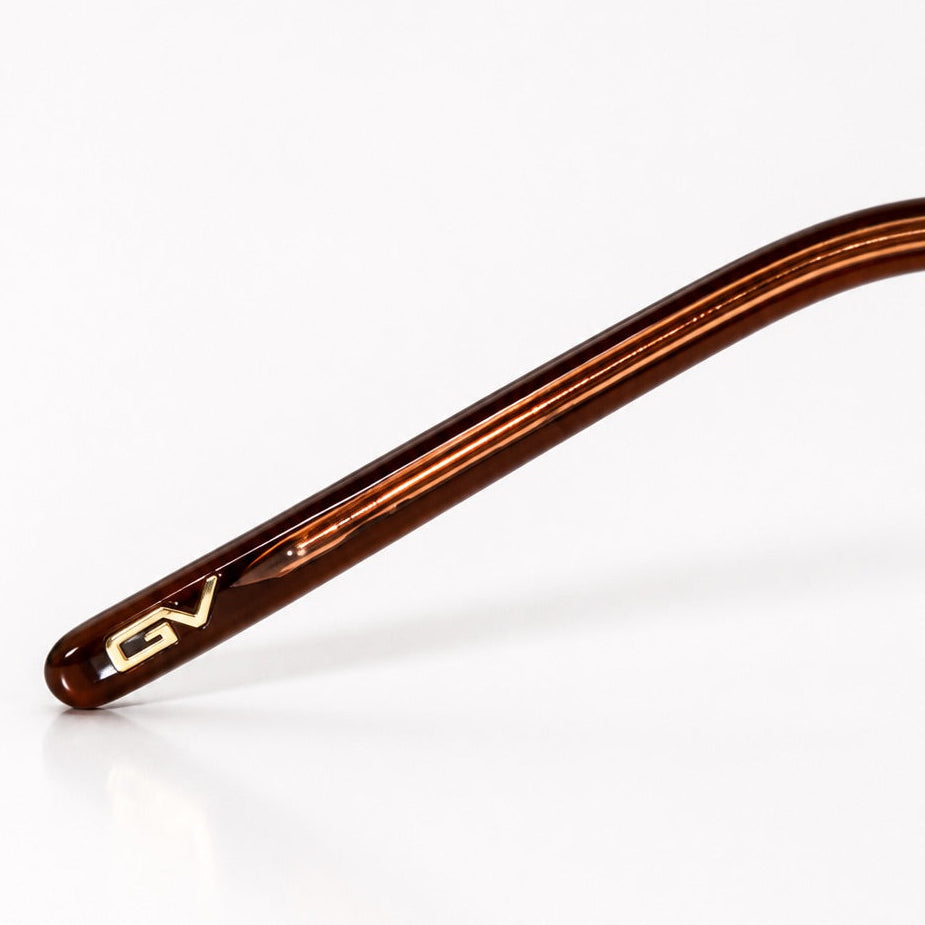 Close-up of a single eyeglass arm in glossy dark brown acetate with a small gold logo detail, photographed on a clean white background.