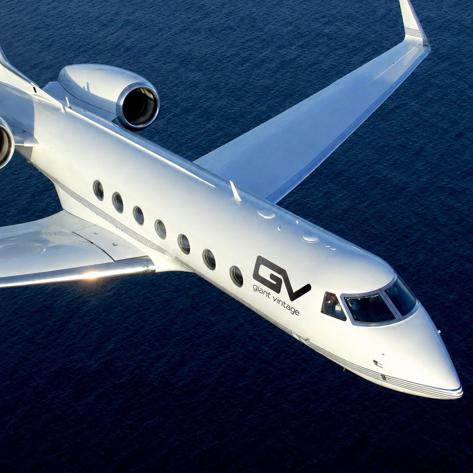 A white Gulfstream business jet photographed from above as it flies over dark blue water, with the Gulfstream logo visible on the side of the fuselage.