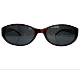Oval sunglasses with a dark brown and black tortoiseshell frame and dark gray tinted lenses, shown against a plain white background.