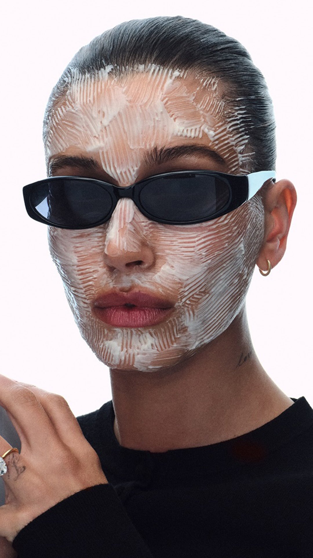 Hailey Bieber wearing a face mask and Daisy sunglasses with a neutral background
