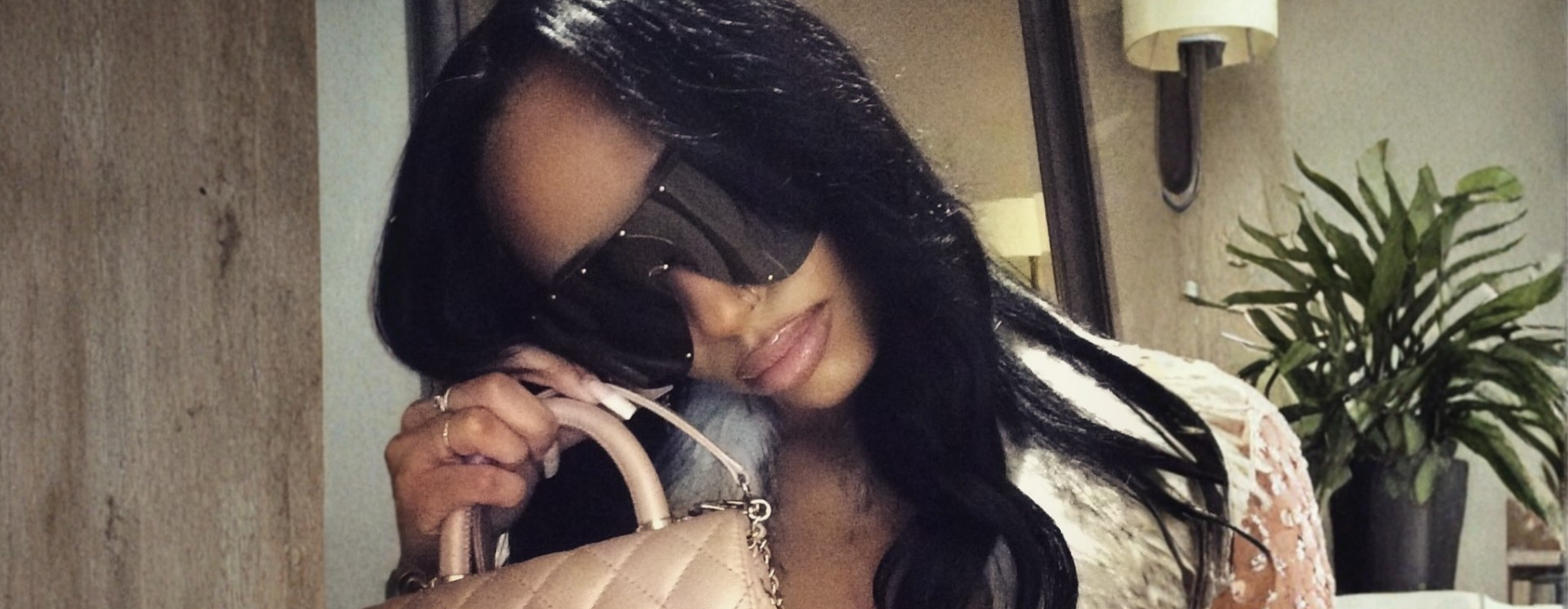 Woman holding a beige handbag indoors with a plant in the background