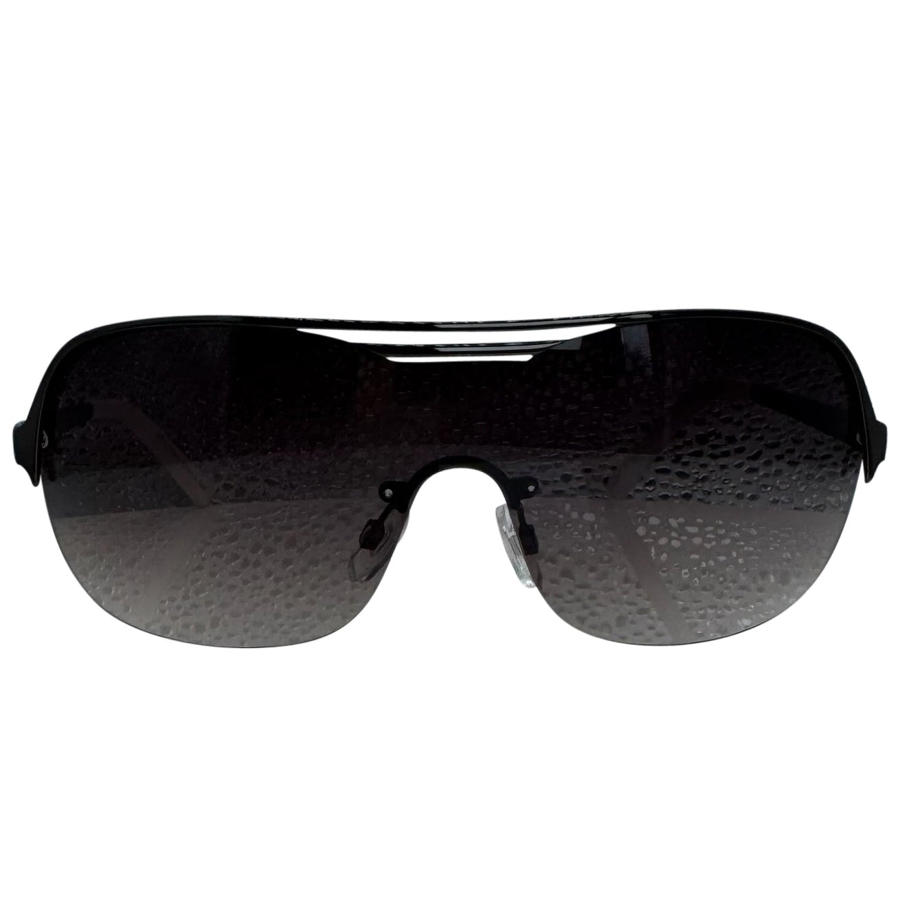 A front-facing product shot of the EXOTIC sunglasses, featuring a rimless shield design with oversized, dark-to-light gradient lenses. The frames are accented by a sleek black double-bridge bar across the top and white arms visible through the lenses.