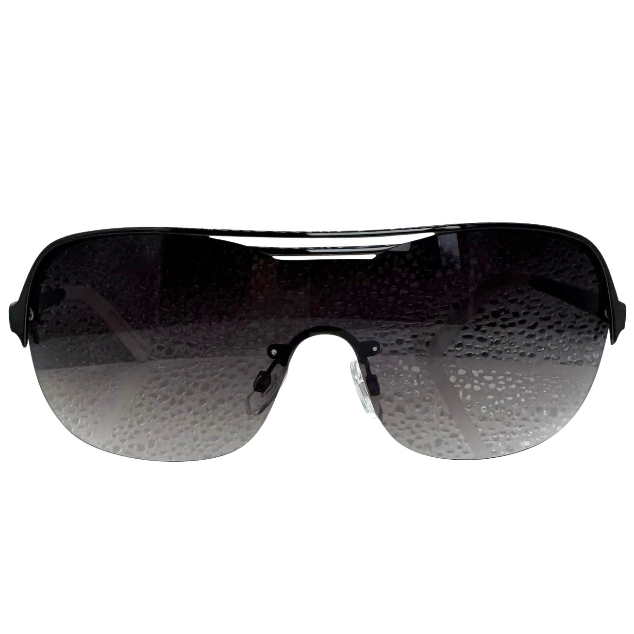 A front-facing product shot of the EXOTIC sunglasses, featuring a rimless shield design with oversized, dark-to-light gradient lenses. The frames are accented by a sleek black double-bridge bar across the top and white arms visible through the lenses.