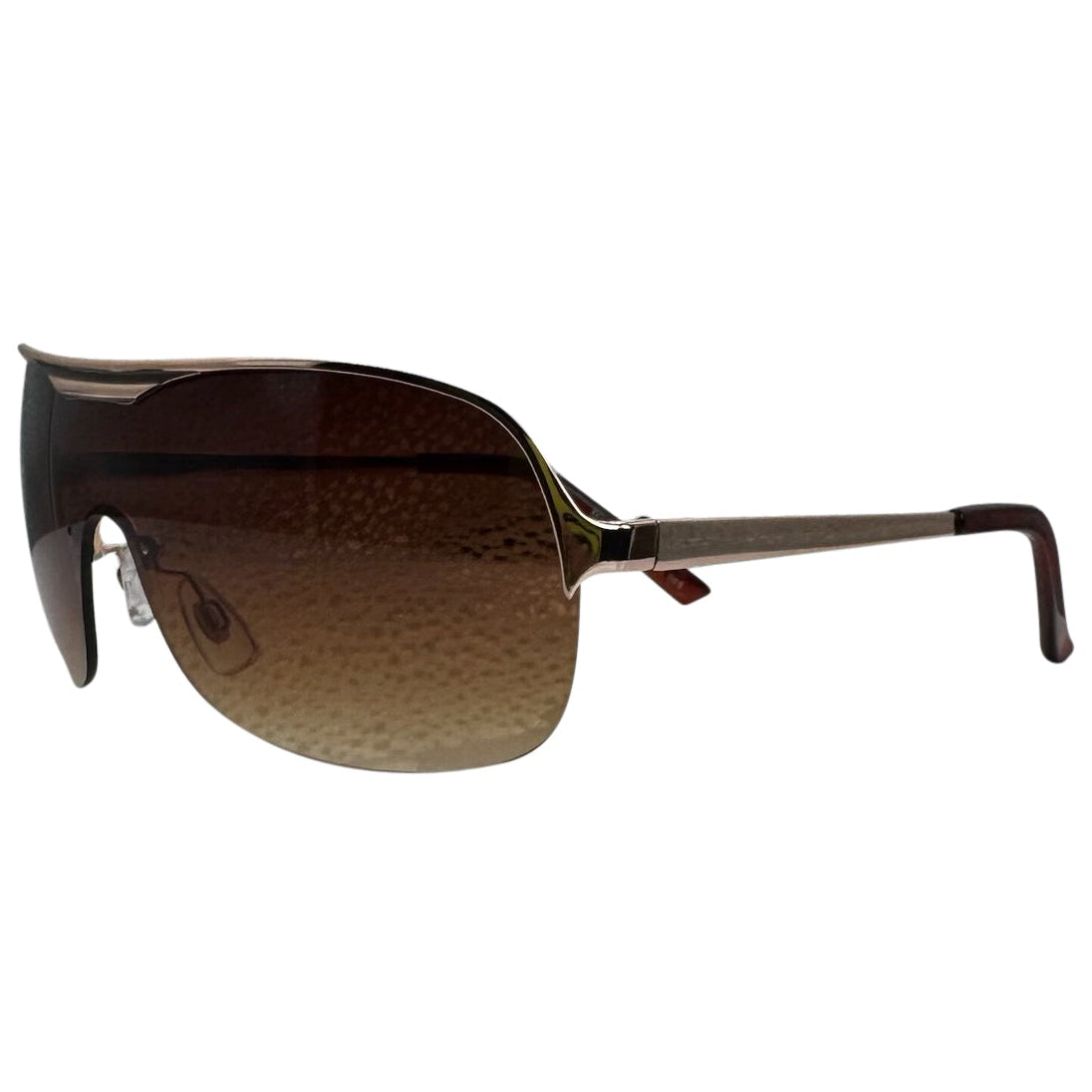 A side4-facing product shot of the EXOTIC sunglasses, featuring a rimless shield design with oversized, dark-to-light gradient lenses. The frames are accented by a sleek brown amber double-bridge bar across the top and white arms visible through the lenses.