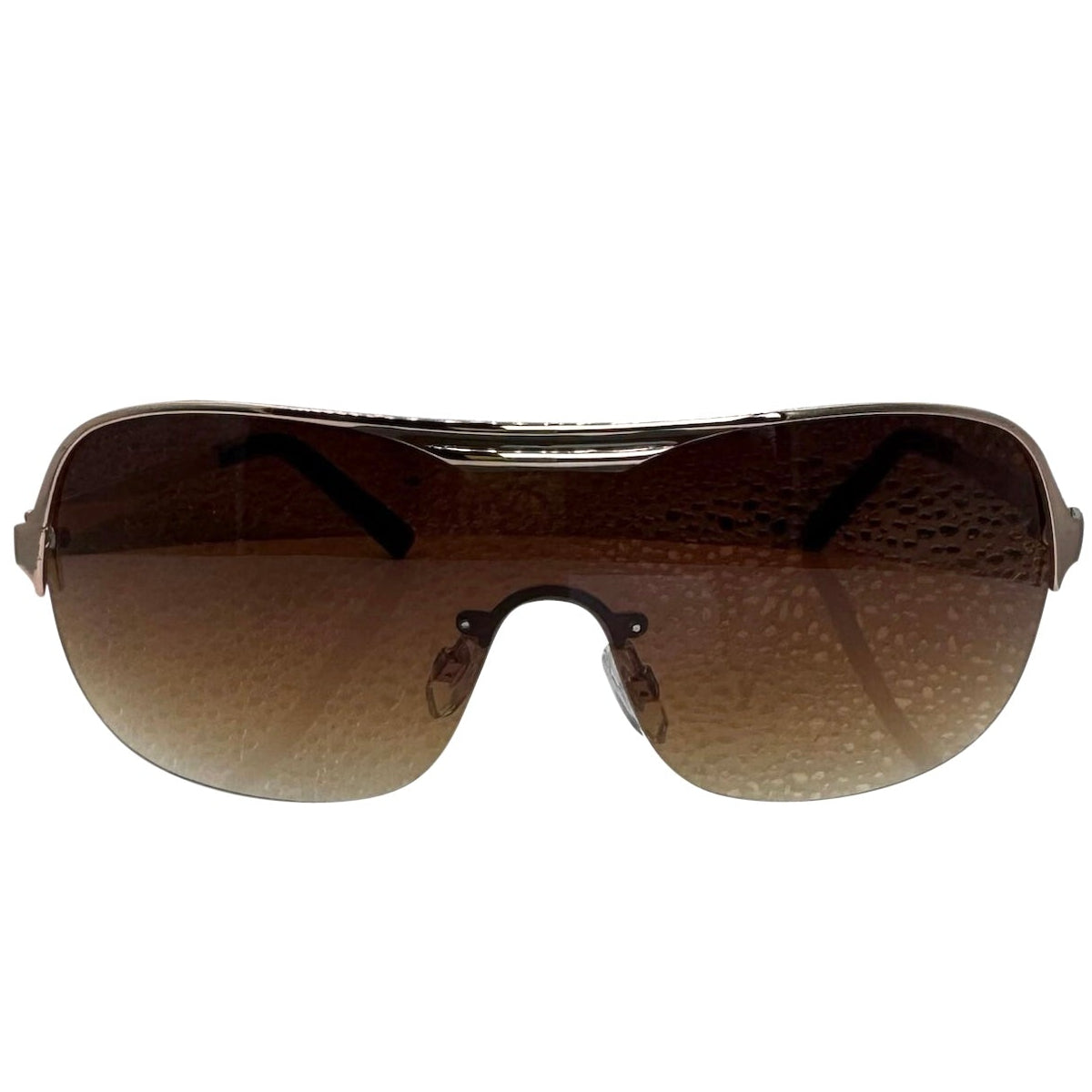 A side-facing product shot of the EXOTIC sunglasses, featuring a rimless shield design with oversized, dark-to-light gradient lenses. The frames are accented by a sleek amber double-bridge bar across the top and silver arms visible through the lenses.