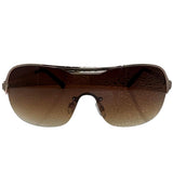 A side-facing product shot of the EXOTIC sunglasses, featuring a rimless shield design with oversized, dark-to-light gradient lenses. The frames are accented by a sleek amber double-bridge bar across the top and silver arms visible through the lenses.
