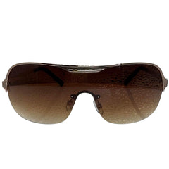 A side-facing product shot of the EXOTIC sunglasses, featuring a rimless shield design with oversized, dark-to-light gradient lenses. The frames are accented by a sleek amber double-bridge bar across the top and silver arms visible through the lenses.