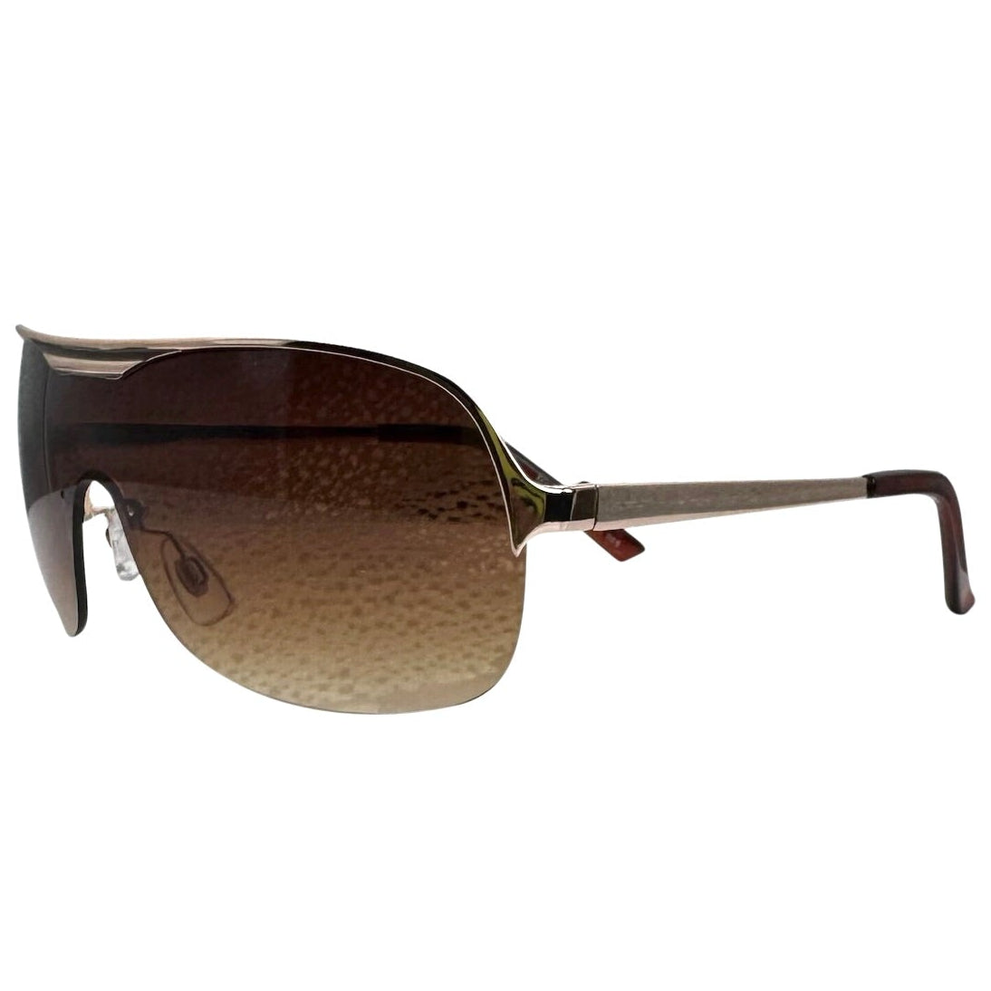 A side-facing product shot of the EXOTIC sunglasses, featuring a rimless shield design with oversized, dark-to-light gradient lenses. The frames are accented by a sleek amber double-bridge bar across the top and silver arms visible through the lenses.