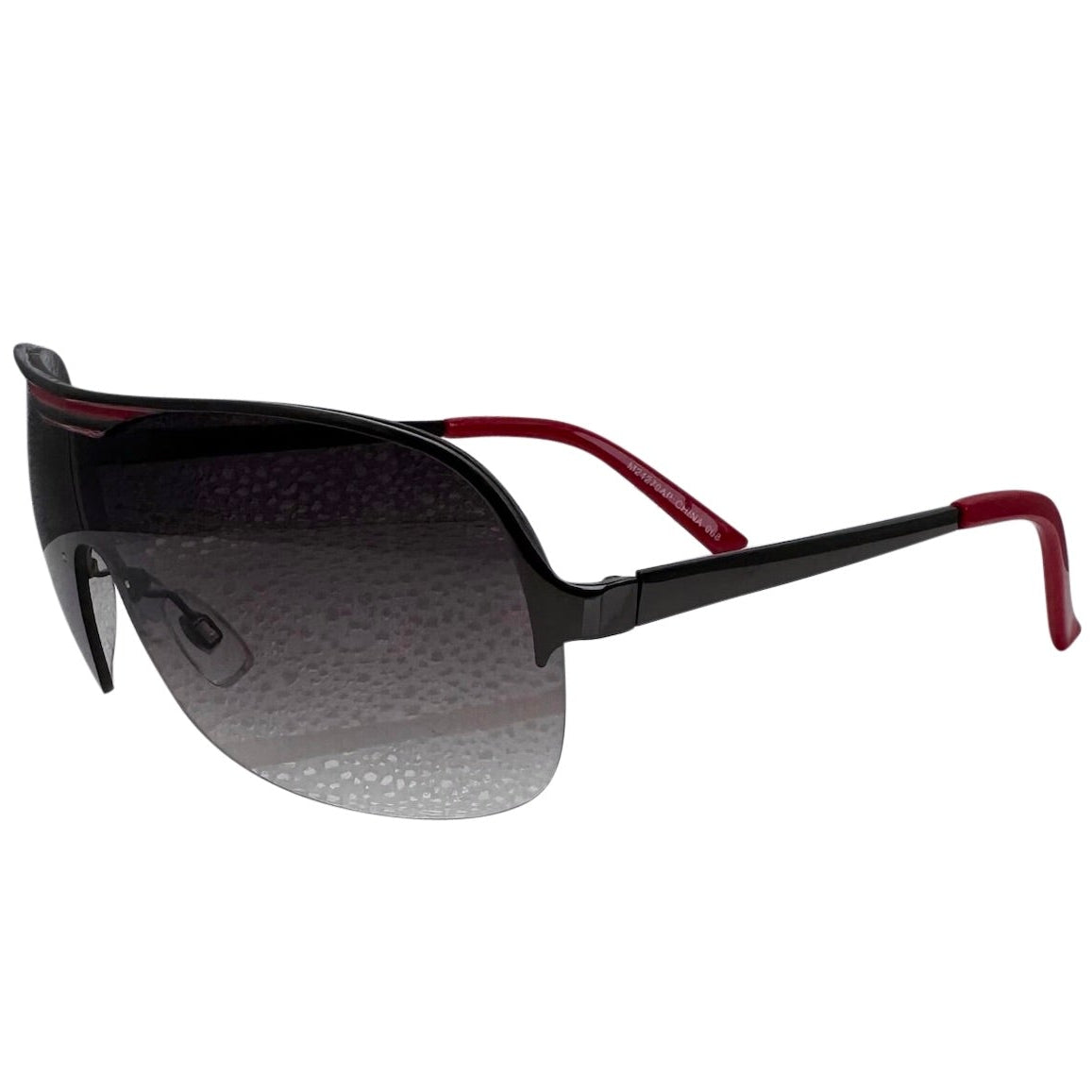A side-facing product shot of the EXOTIC sunglasses, featuring a rimless shield design with oversized, dark-to-light gradient lenses. The frames are accented by a sleek red double-bridge bar across the top and red arms visible through the lenses.