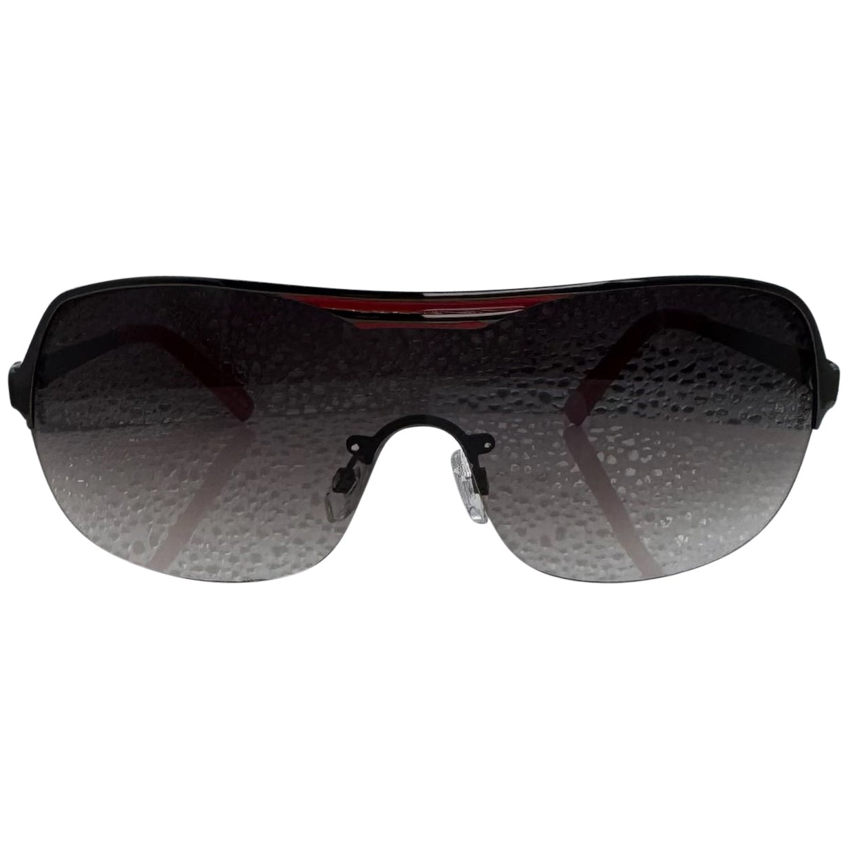 A front-facing product shot of the EXOTIC sunglasses, featuring a rimless shield design with oversized, dark-to-light gradient lenses. The frames are accented by a sleek red/ black double-bridge bar across the top and white arms visible through the lenses.
