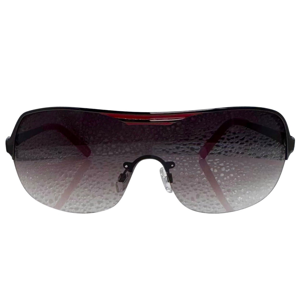 A front-facing product shot of the EXOTIC sunglasses, featuring a rimless shield design with oversized, dark-to-light gradient lenses. The frames are accented by a sleek red double-bridge bar across the top and red arms visible through the lenses.