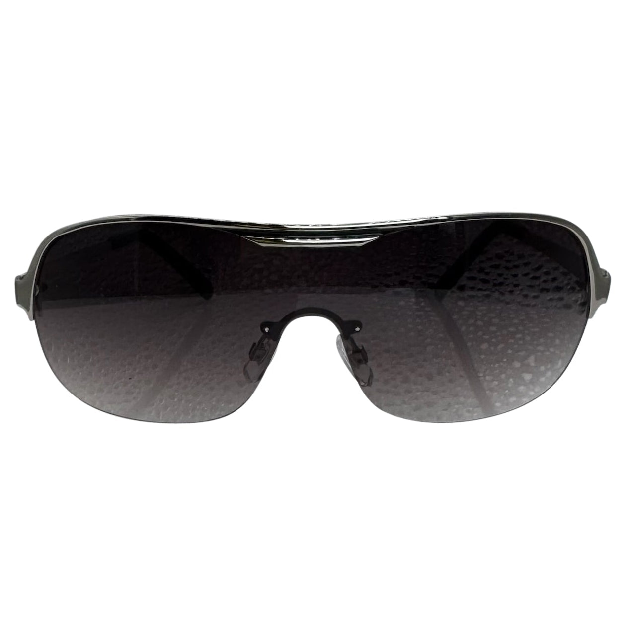 A front-facing product shot of the EXOTIC sunglasses, featuring a rimless shield design with oversized, dark-to-light gradient lenses. The frames are accented by a sleek silver double-bridge bar across the top and white arms visible through the lenses.