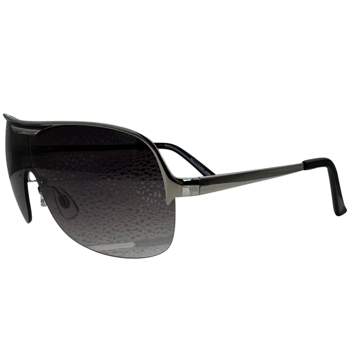 A side-facing product shot of the EXOTIC sunglasses, featuring a rimless shield design with oversized, dark-to-light gradient lenses. The frames are accented by a sleek black double-bridge bar across the top and white arms visible through the lenses.