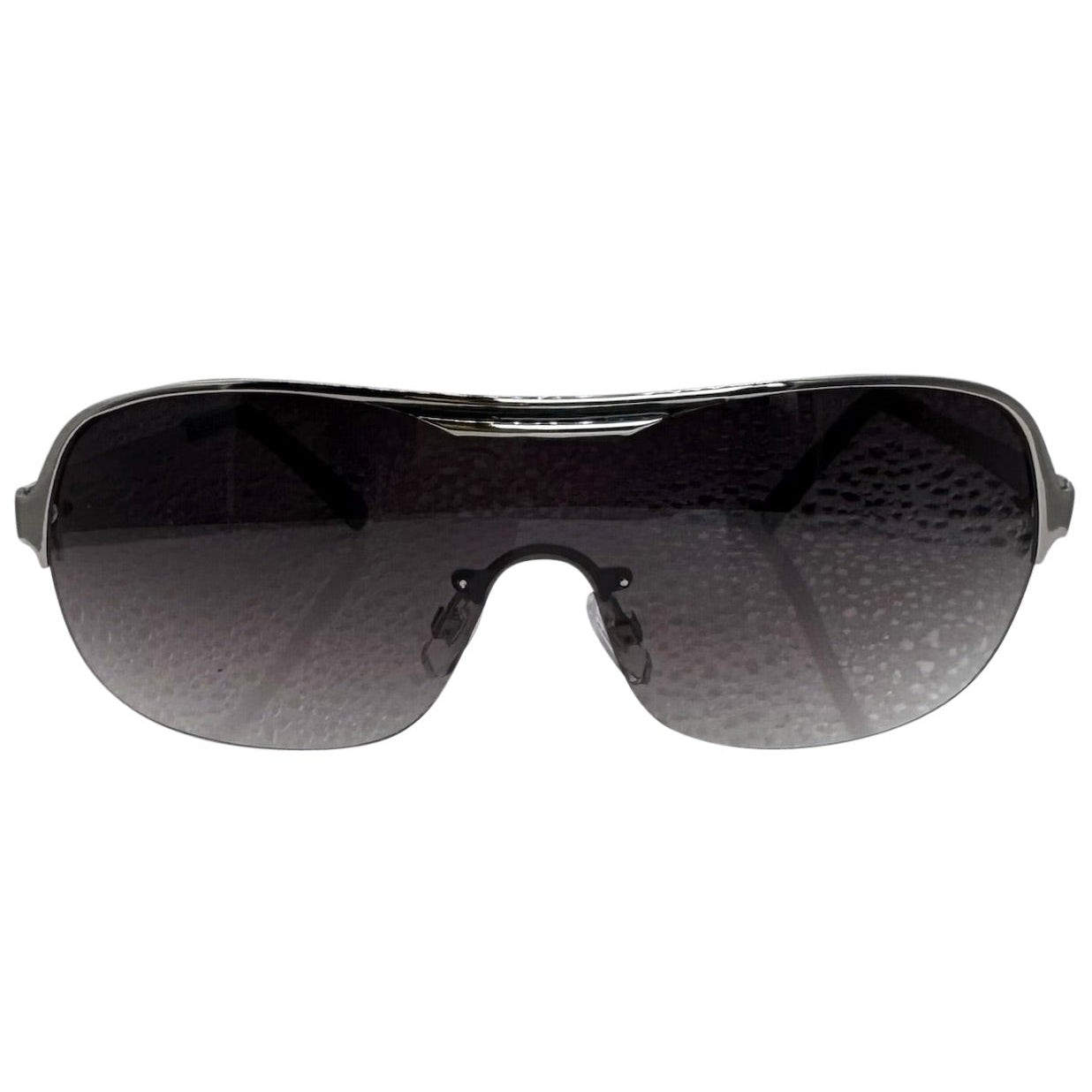 A front-facing product shot of the EXOTIC sunglasses, featuring a rimless shield design with oversized, dark-to-light gradient lenses. The frames are accented by a sleek silver double-bridge bar across the top and silver arms visible through the lenses.