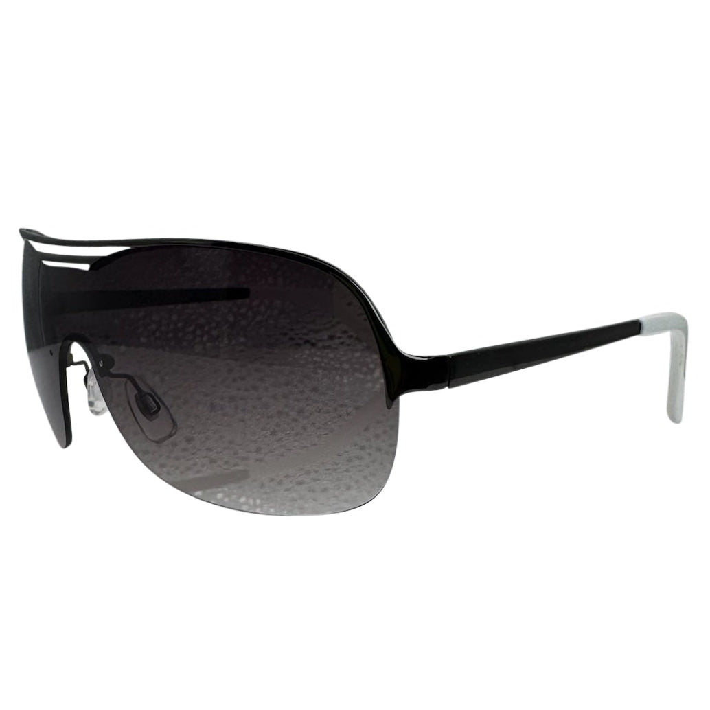 A front-facing product shot of the EXOTIC sunglasses, featuring a rimless shield design with oversized, dark-to-light gradient lenses. The frames are accented by a sleek silver double-bridge bar across the top and white arms visible through the lenses.