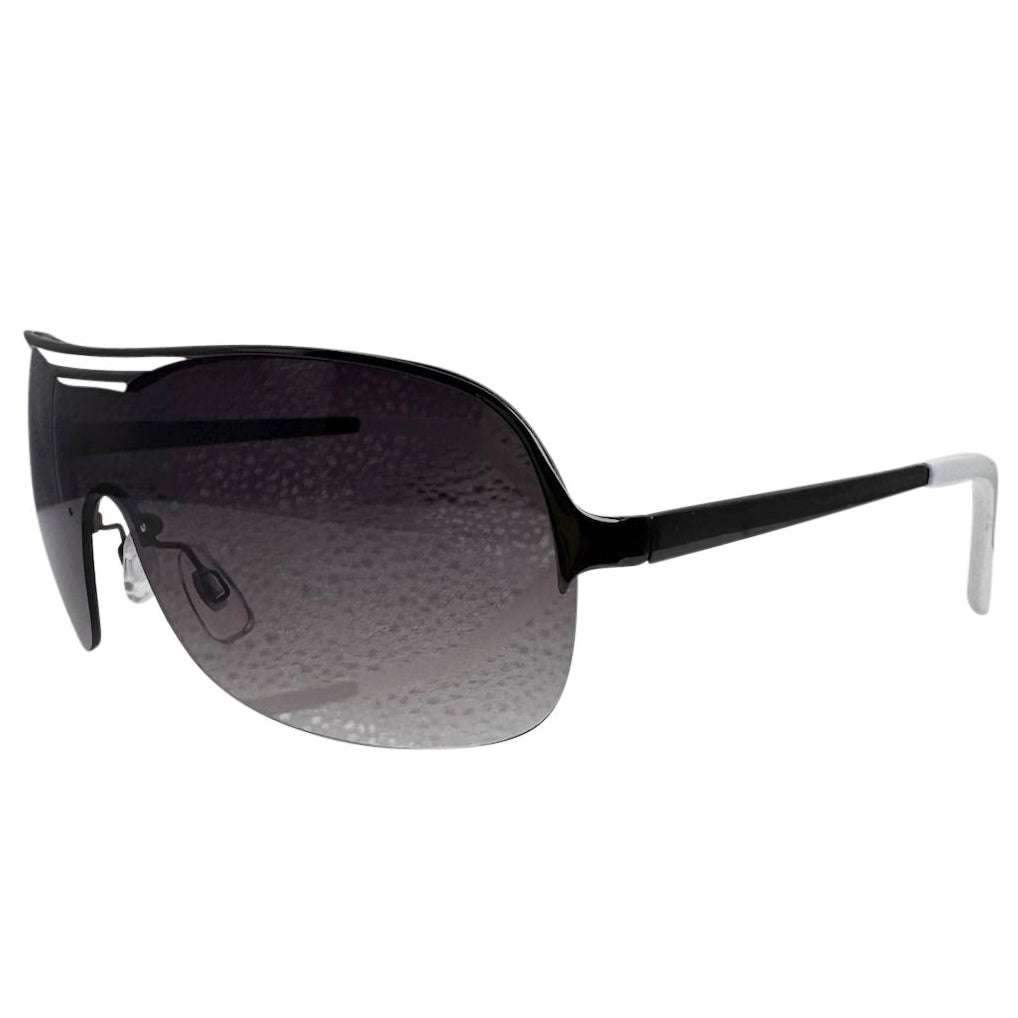 A side-facing product shot of the EXOTIC sunglasses, featuring a rimless shield design with oversized, dark-to-light gradient lenses. The frames are accented by a sleek black double-bridge bar across the top and white arms visible through the lenses.