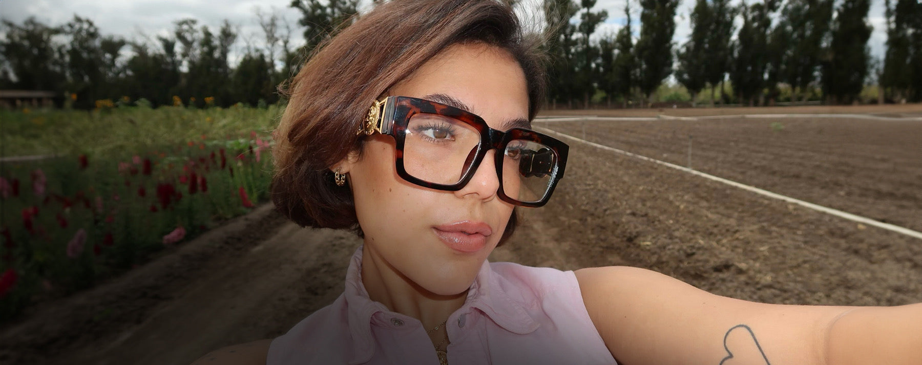 Model wearing square oversized clear glasses in tortoise on a flower and produce farm 
