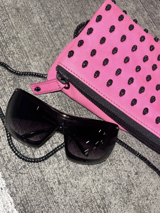 Instagram post showing Black sunglasses on a pink polka dot pouch with a chain strap on a gray surface