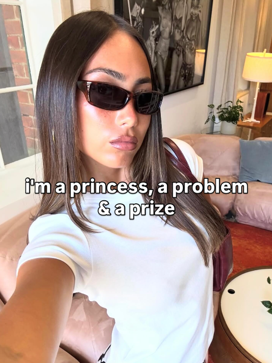 Person wearing sunglasses with text 'i'm a princess, a problem & a prize' in a living room setting.