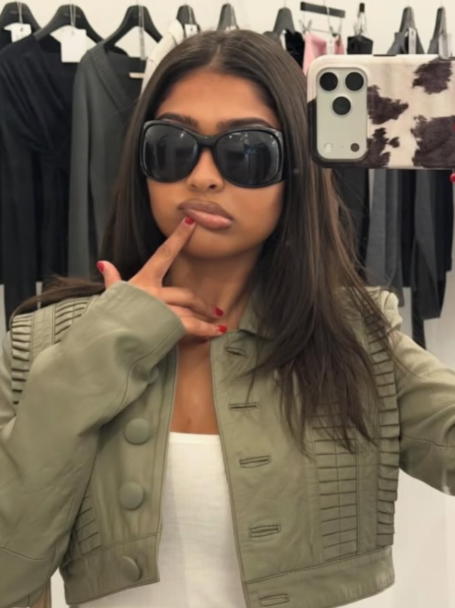 Person wearing sunglasses and a green jacket in a clothing store