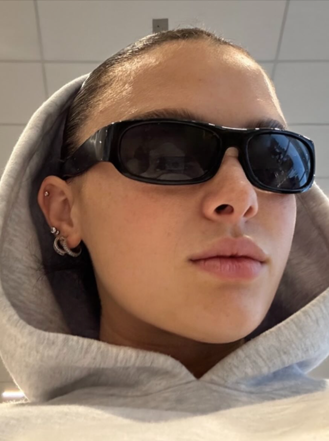 Person wearing sunglasses and a gray hoodie indoors