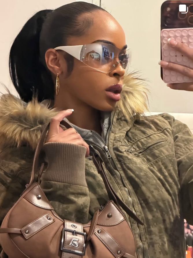 Person wearing a green jacket with a fur-lined hood, holding a brown handbag.