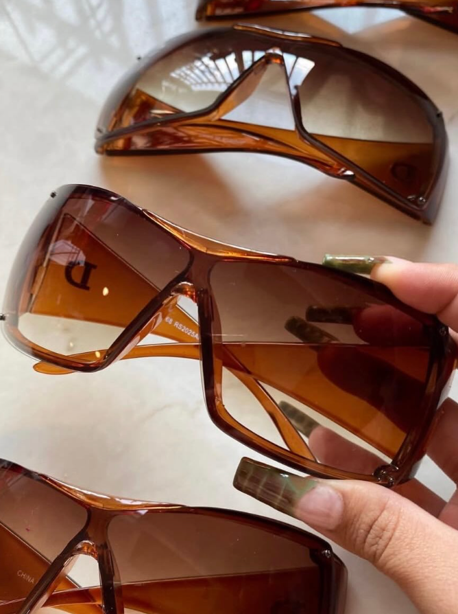 Brown sunglasses on a white surface with a hand holding one of them.