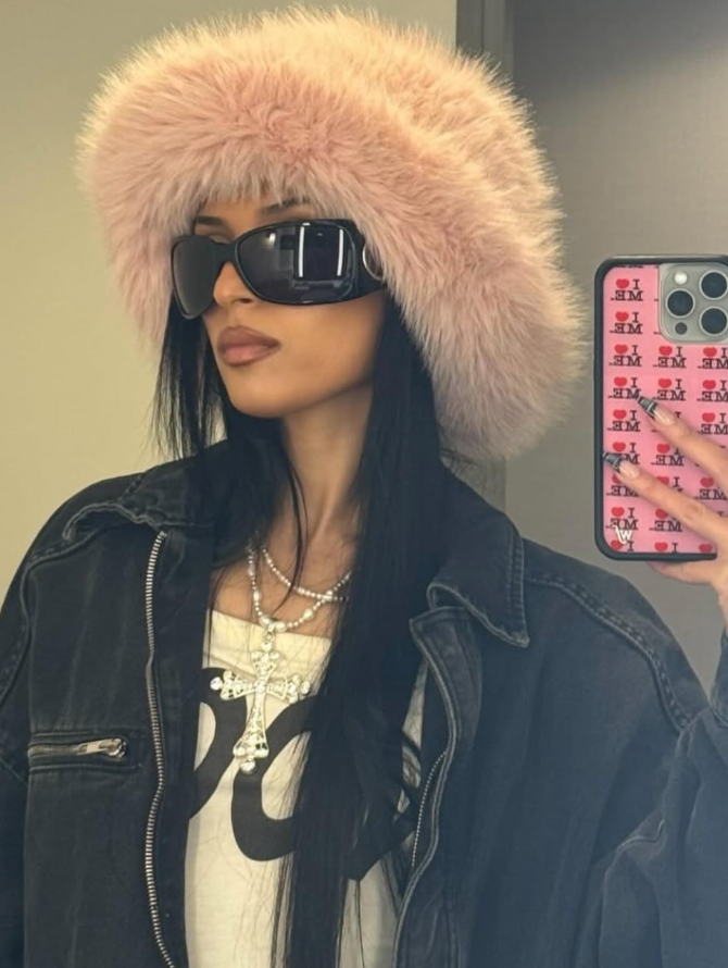 Person wearing a fluffy pink hat and sunglasses, holding a phone with a colorful case.