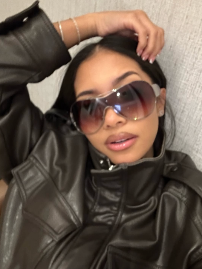 Person wearing a black leather jacket and sunglasses with a neutral background