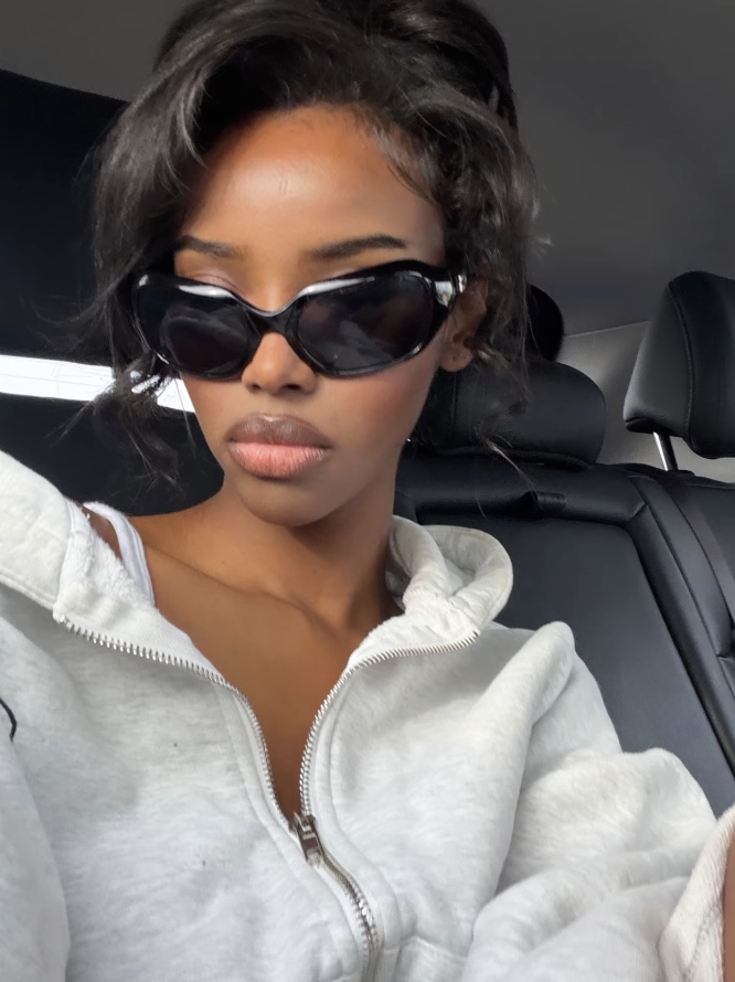 Woman wearing sunglasses and a white jacket inside a car