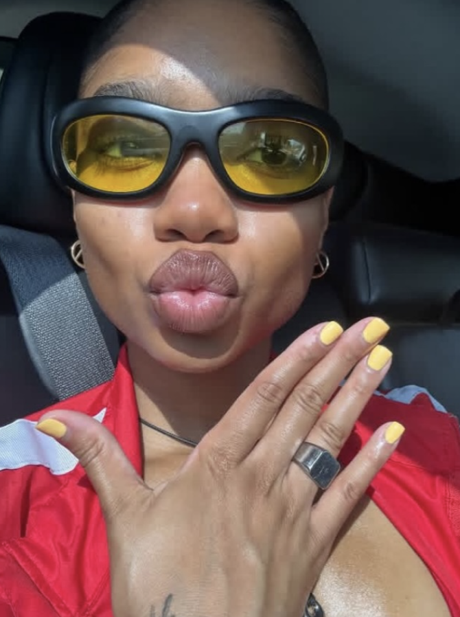 Person wearing yellow-tinted sunglasses and a red jacket inside a vehicle.