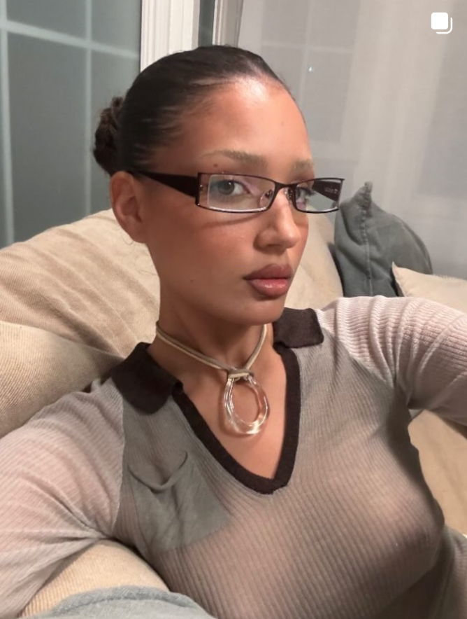 Woman wearing glasses and a gray sweater sitting on a couch.