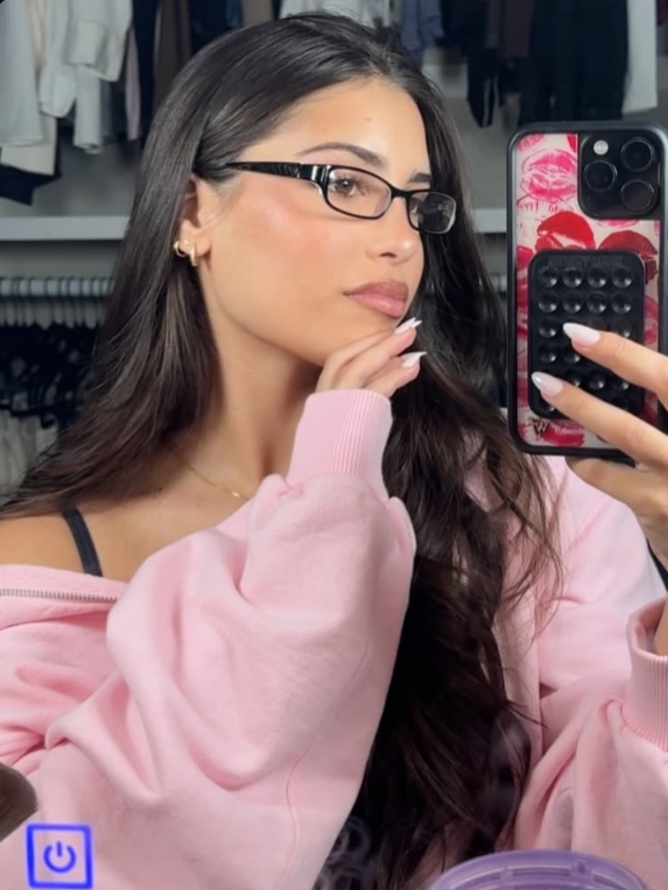 Woman taking a mirror selfie wearing a pink sweatshirt in a clothing store.