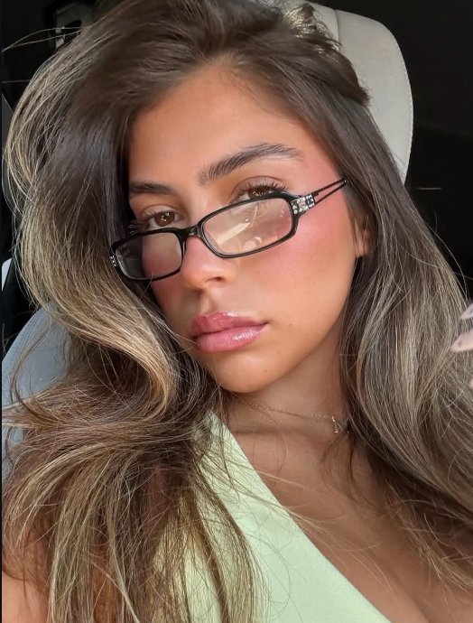 Close-up of a person with glasses and long hair, wearing a light green top.
