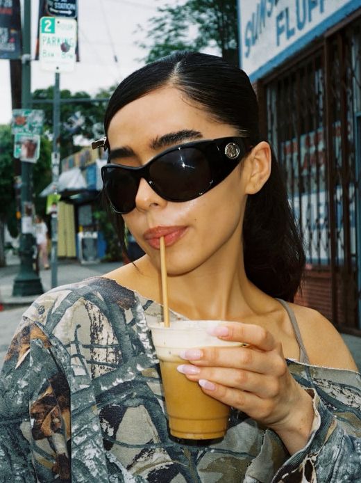 Woman drinking from a coffee cup outdoors with a city street background